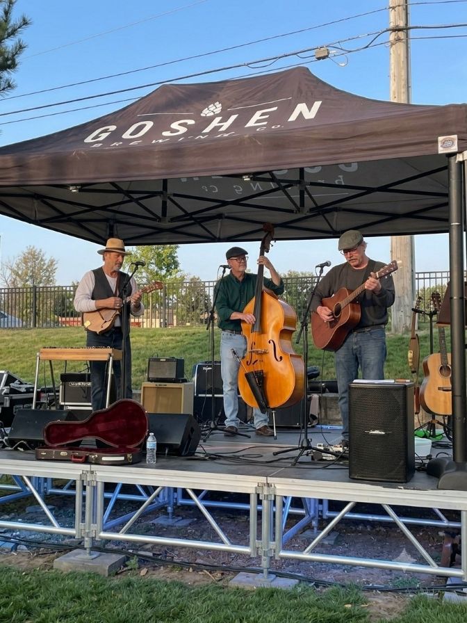 The Dawg band performs on an elevated outdoor stage under a black canopy tent labeled "Goshen Brewing Co."
